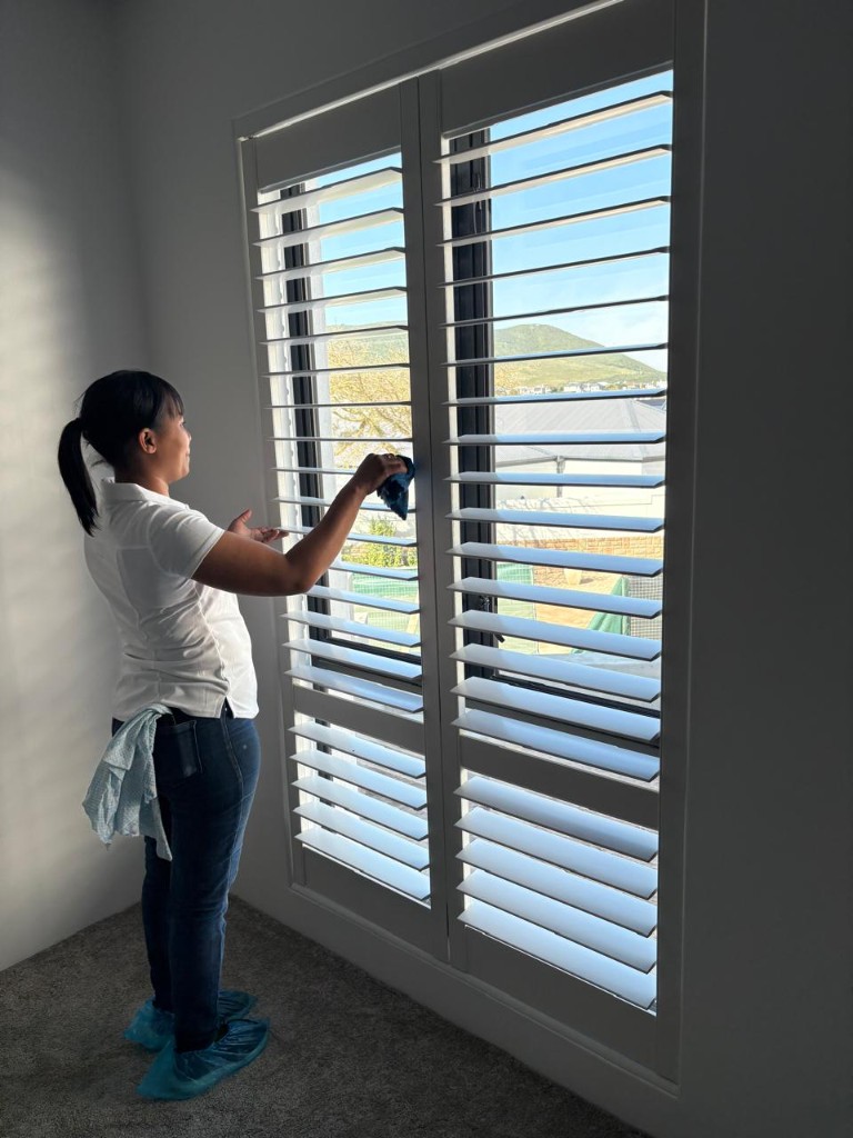 West Coast Cleaners team member cleaning plantation shutters in a home